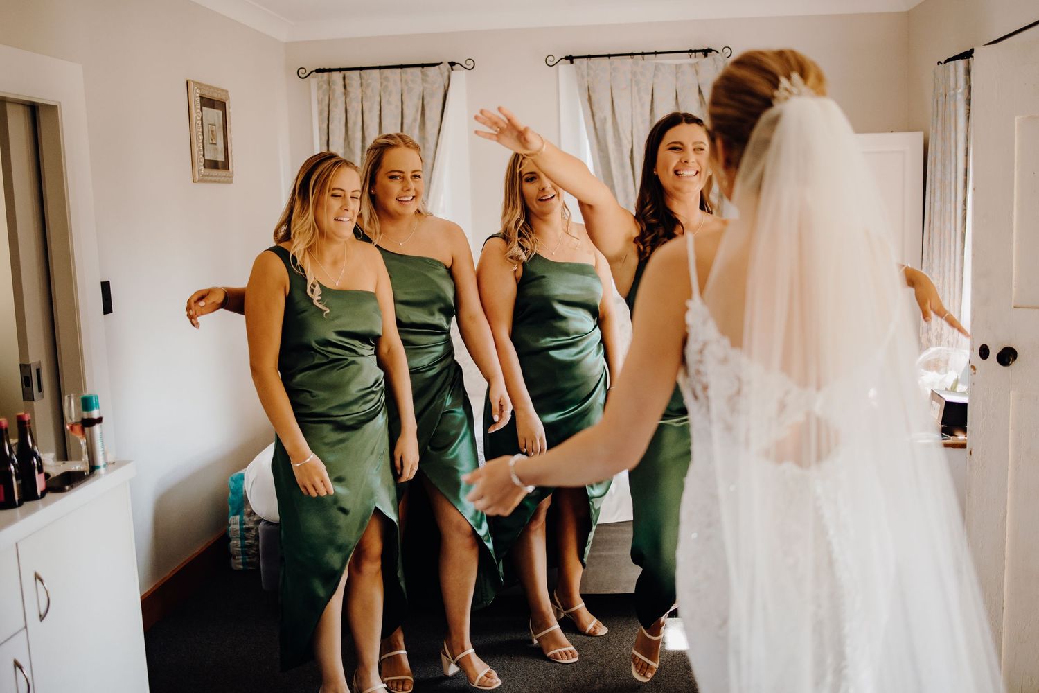 Bridesmaids in elegant green dresses stand together during wedding preparations.