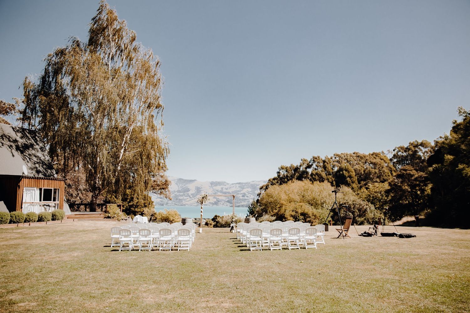 Outdoor wedding ceremony setup with white chairs on lawn overlooking water view.