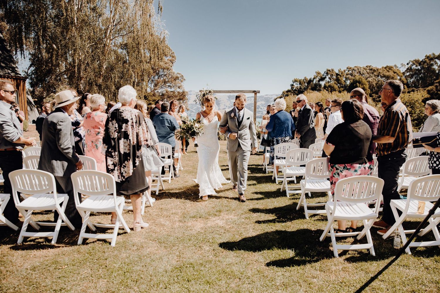 Wedding ceremony processional with guests standing along white chair-lined aisle.