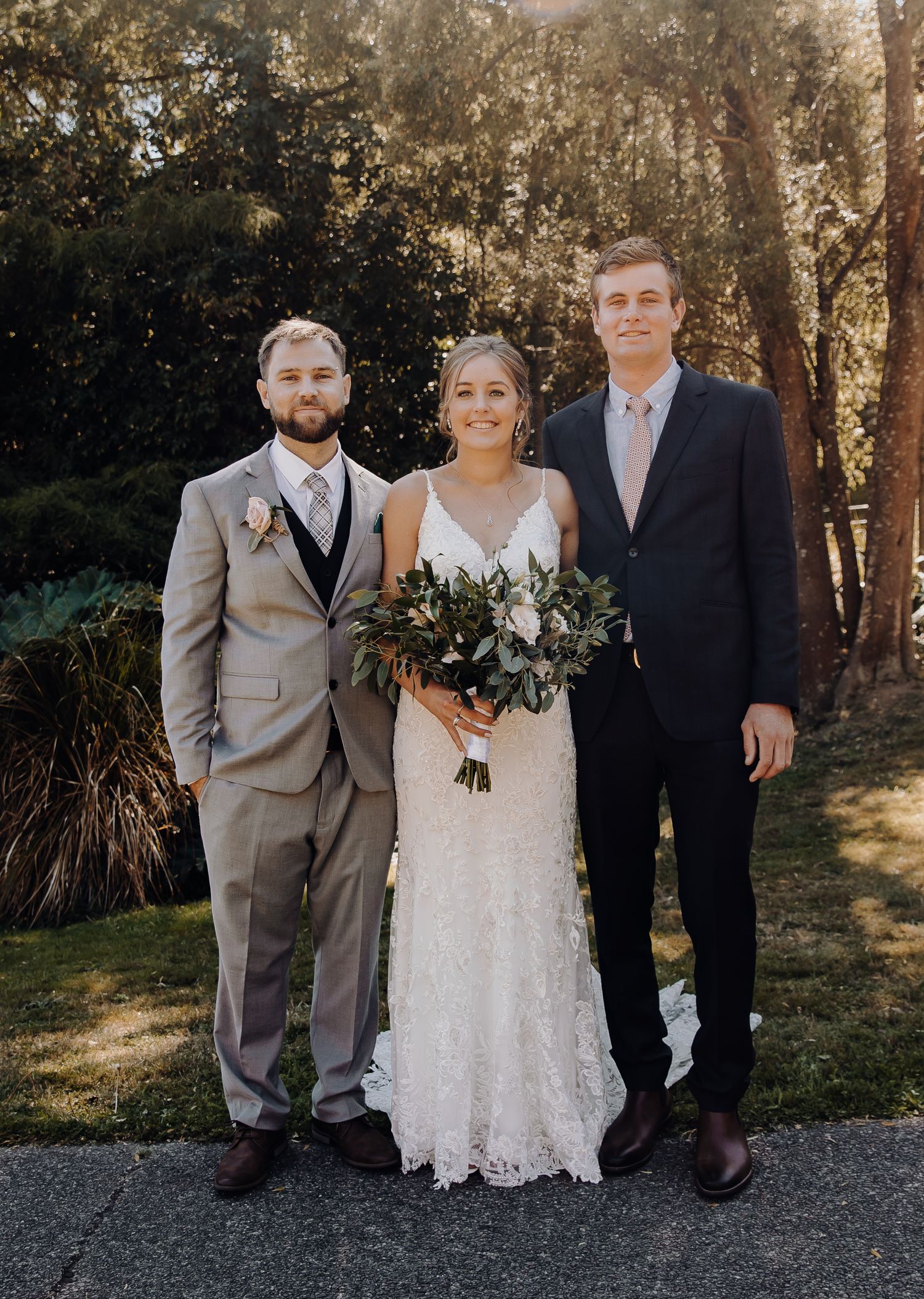 Wedding party poses for formal portrait outdoors with trees in background.