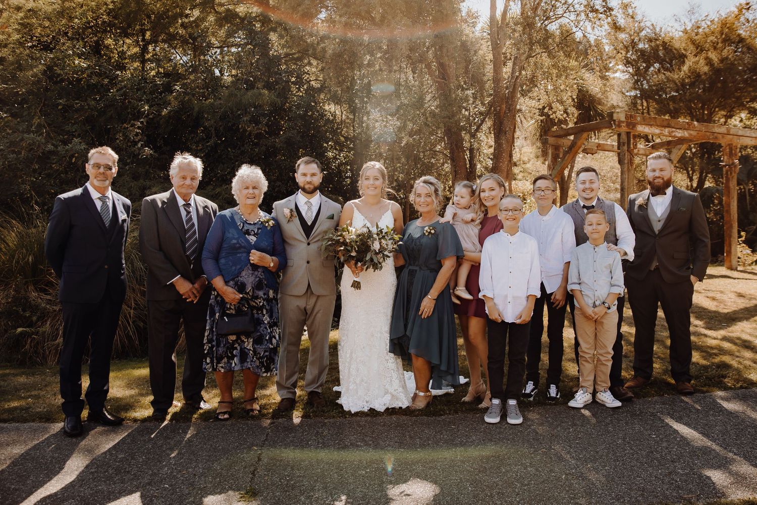 Large wedding party group photo featuring the newlyweds with family members outdoors.