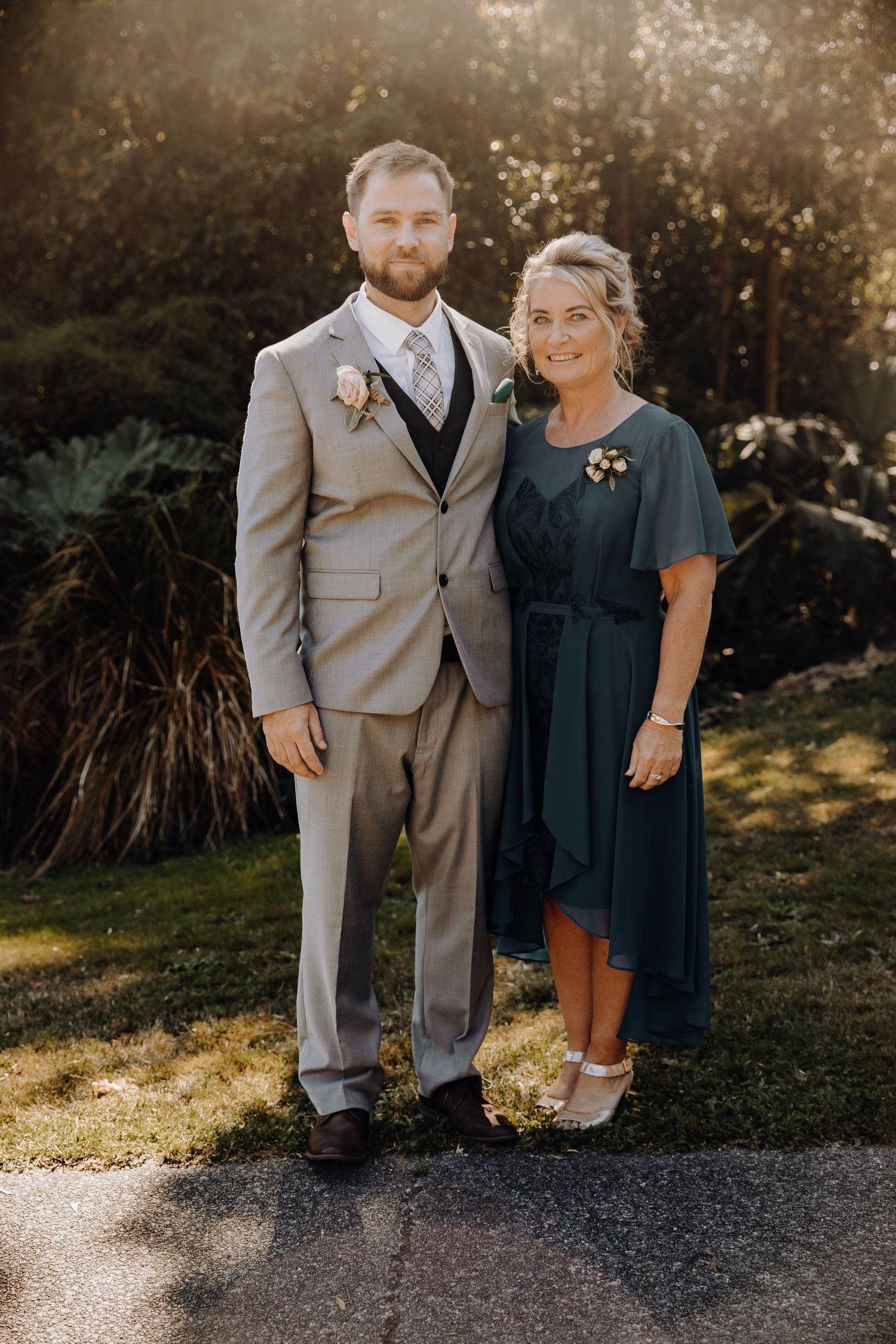 Wedding guest pair in formal attire pose together in natural outdoor setting.