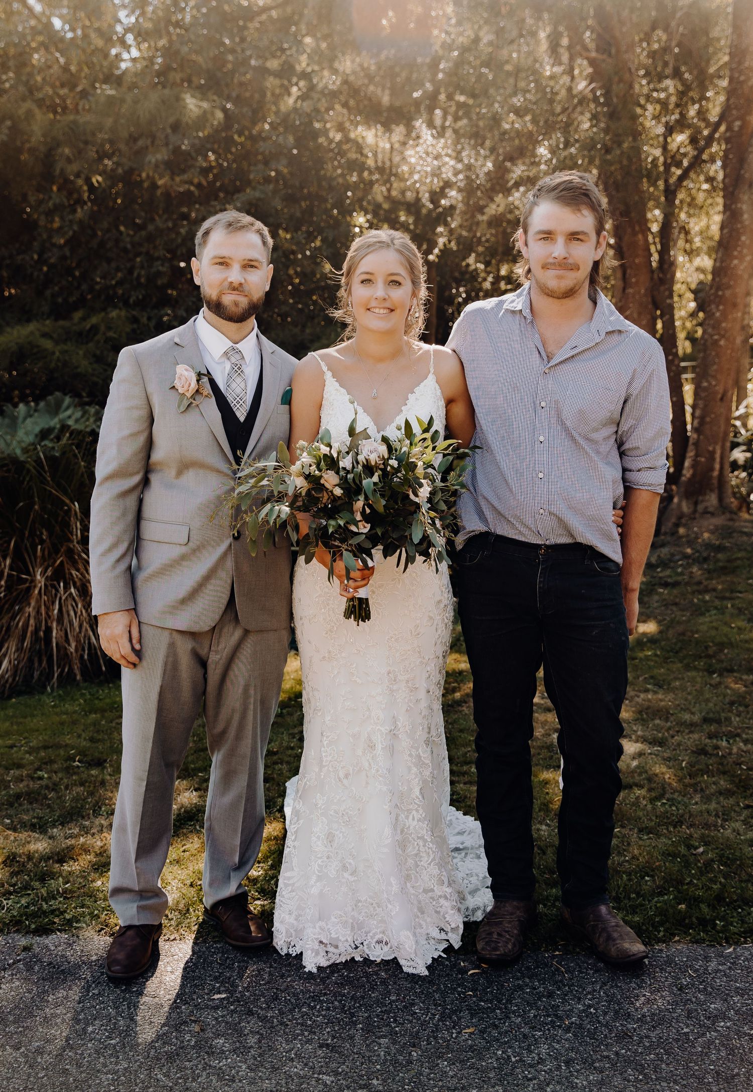 Three wedding guests pose together outdoors with the bride holding a floral bouquet.