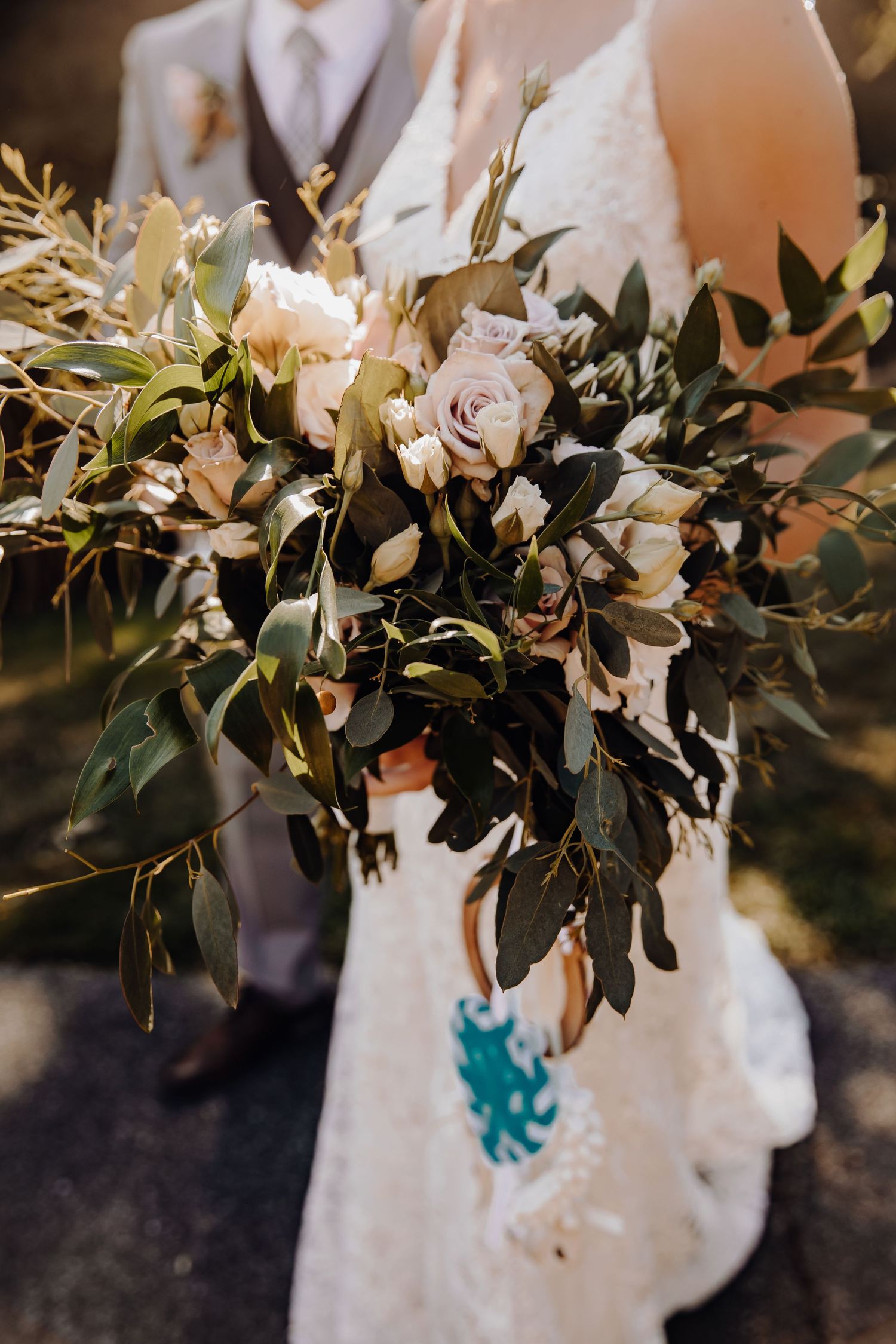 Close-up of an elegant wedding bouquet with roses and greenery against a white dress.