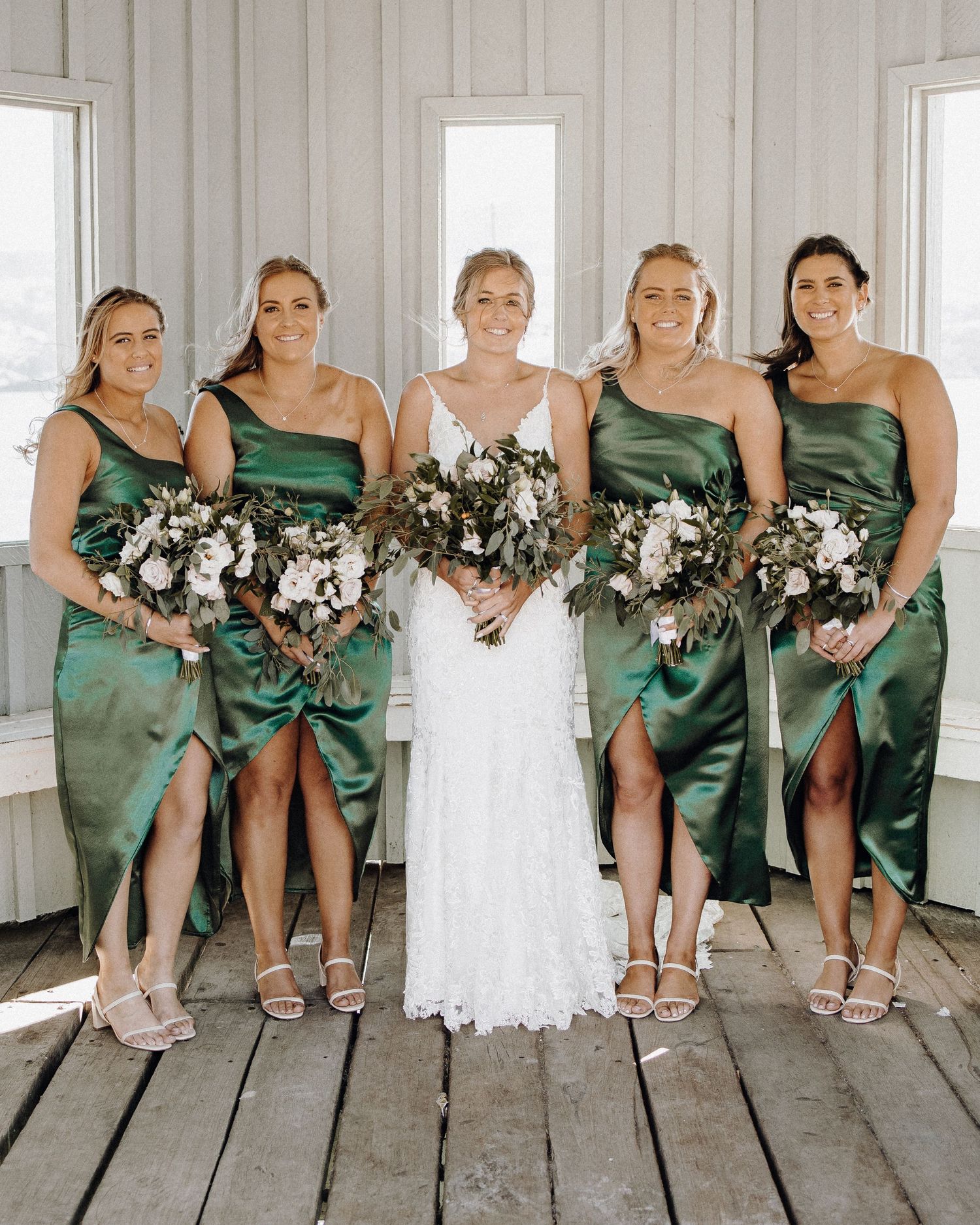 Bridesmaids in matching emerald green dresses pose with bride in white gown.