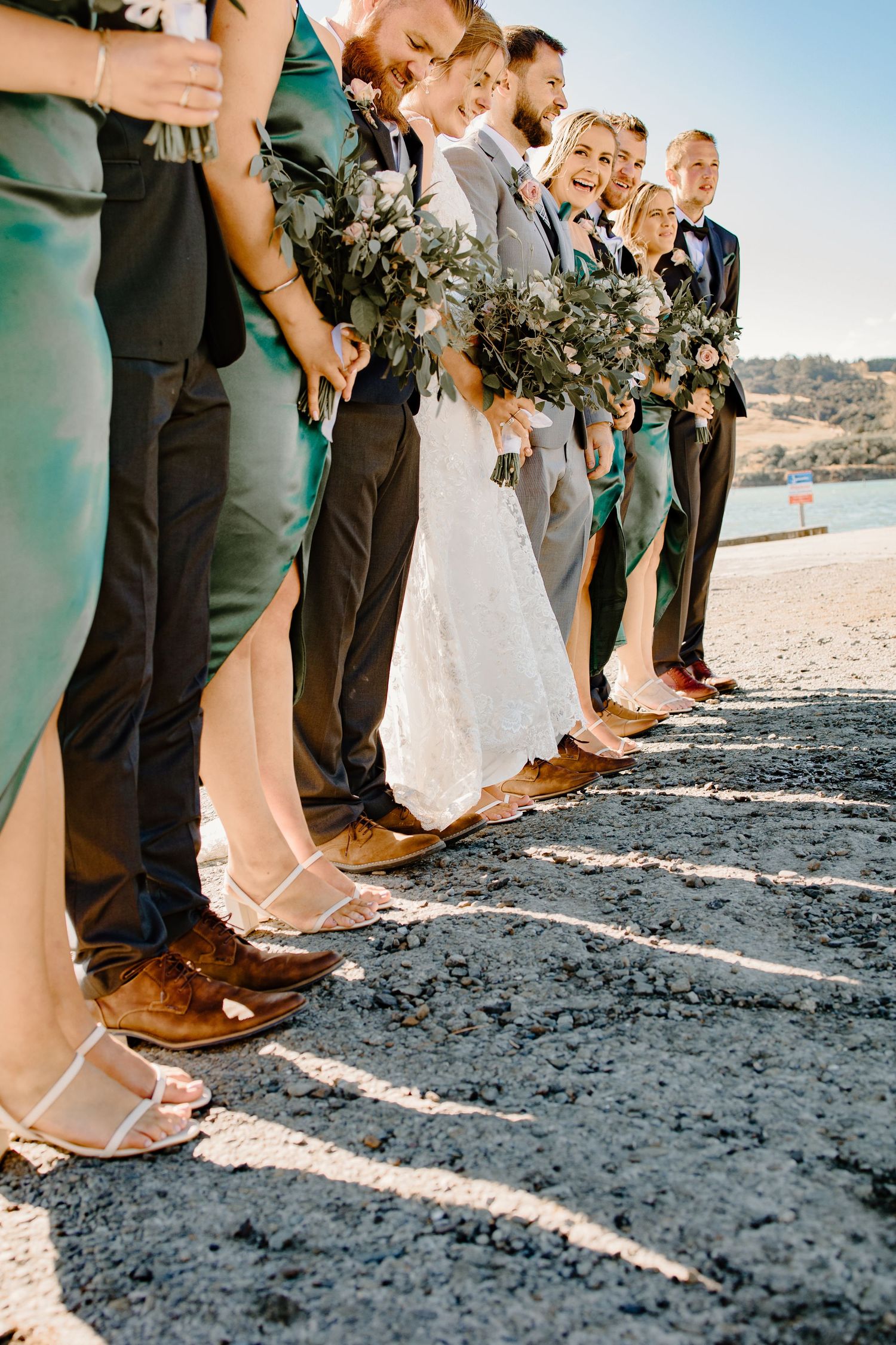 Wedding party members' feet lined up on beach showing dress shoes and formal attire.