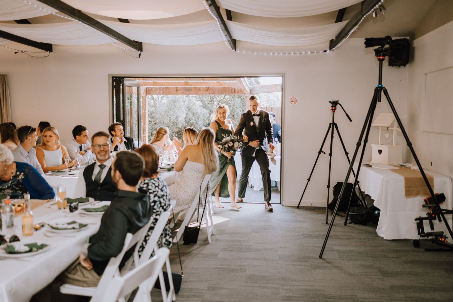 Wedding guests seated at tables watch as newlyweds make their reception entrance.