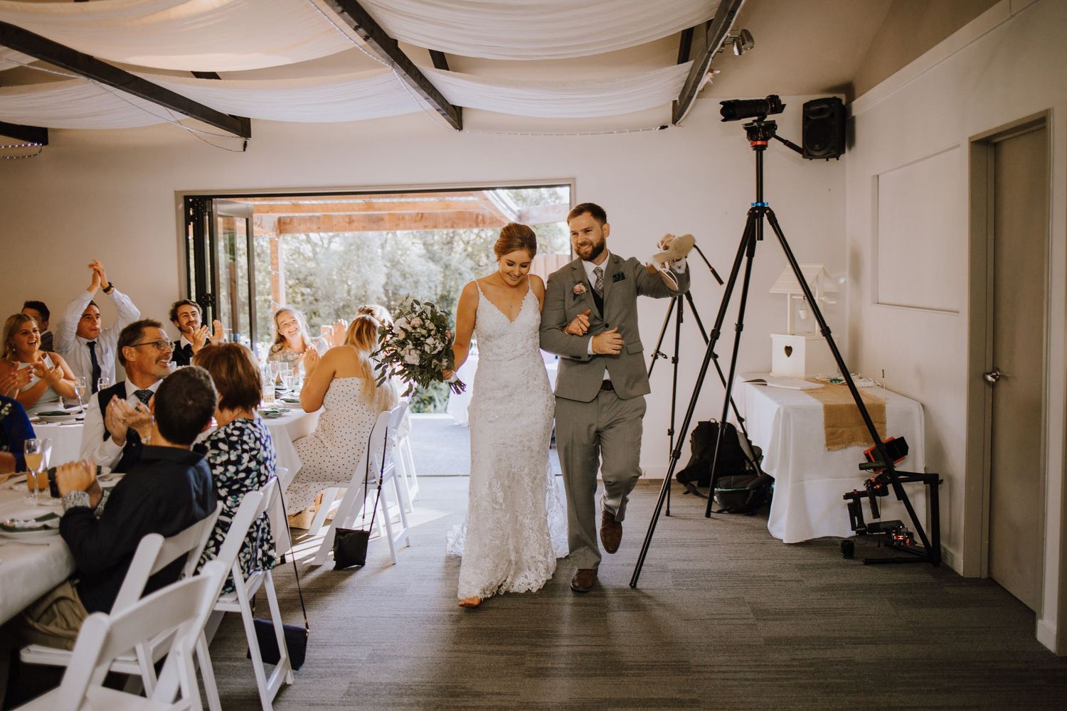 Wedding guests cheer as the couple walks down the aisle in a bright indoor venue.
