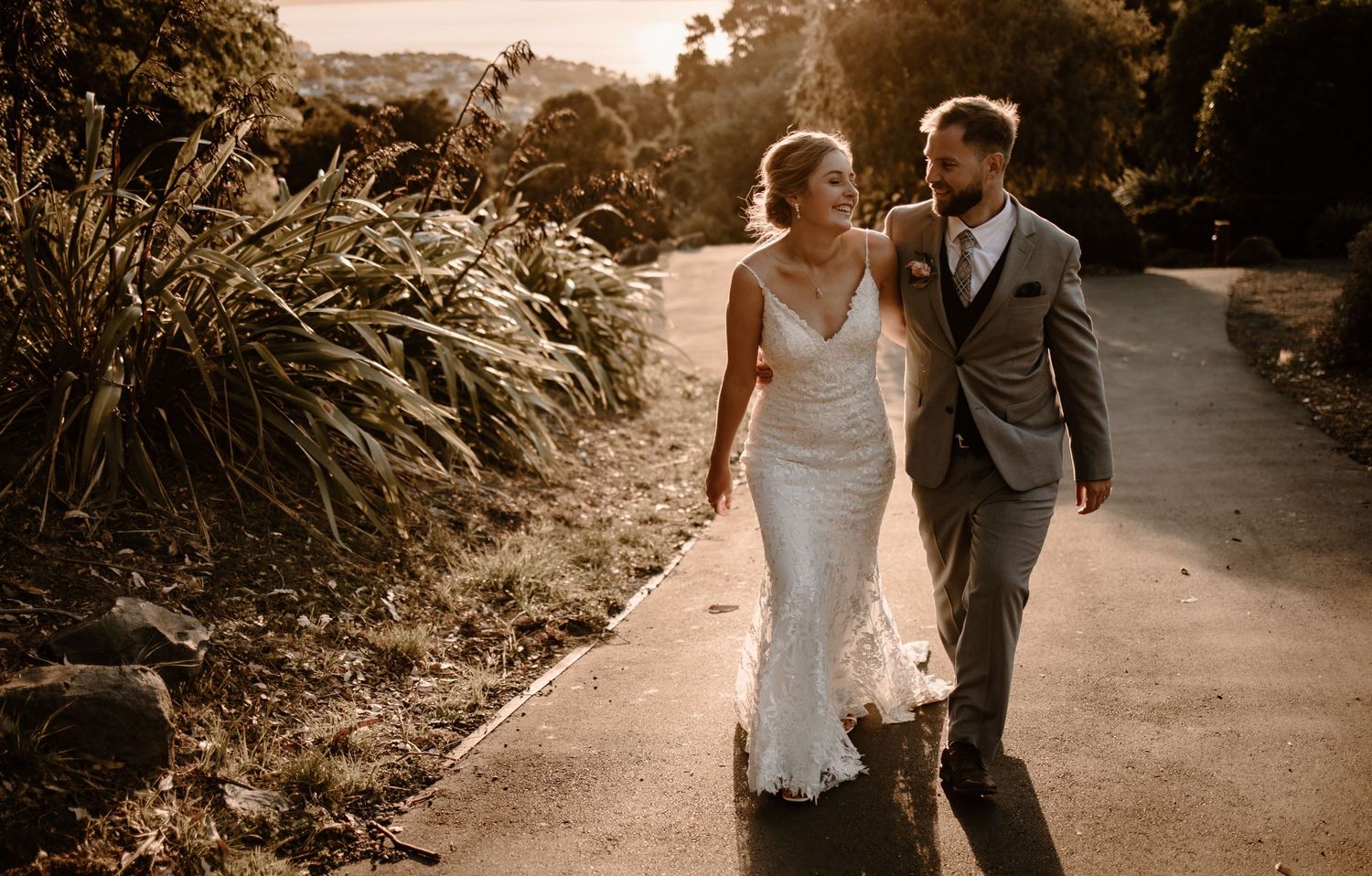 Newlyweds walk together on a garden path during golden hour.