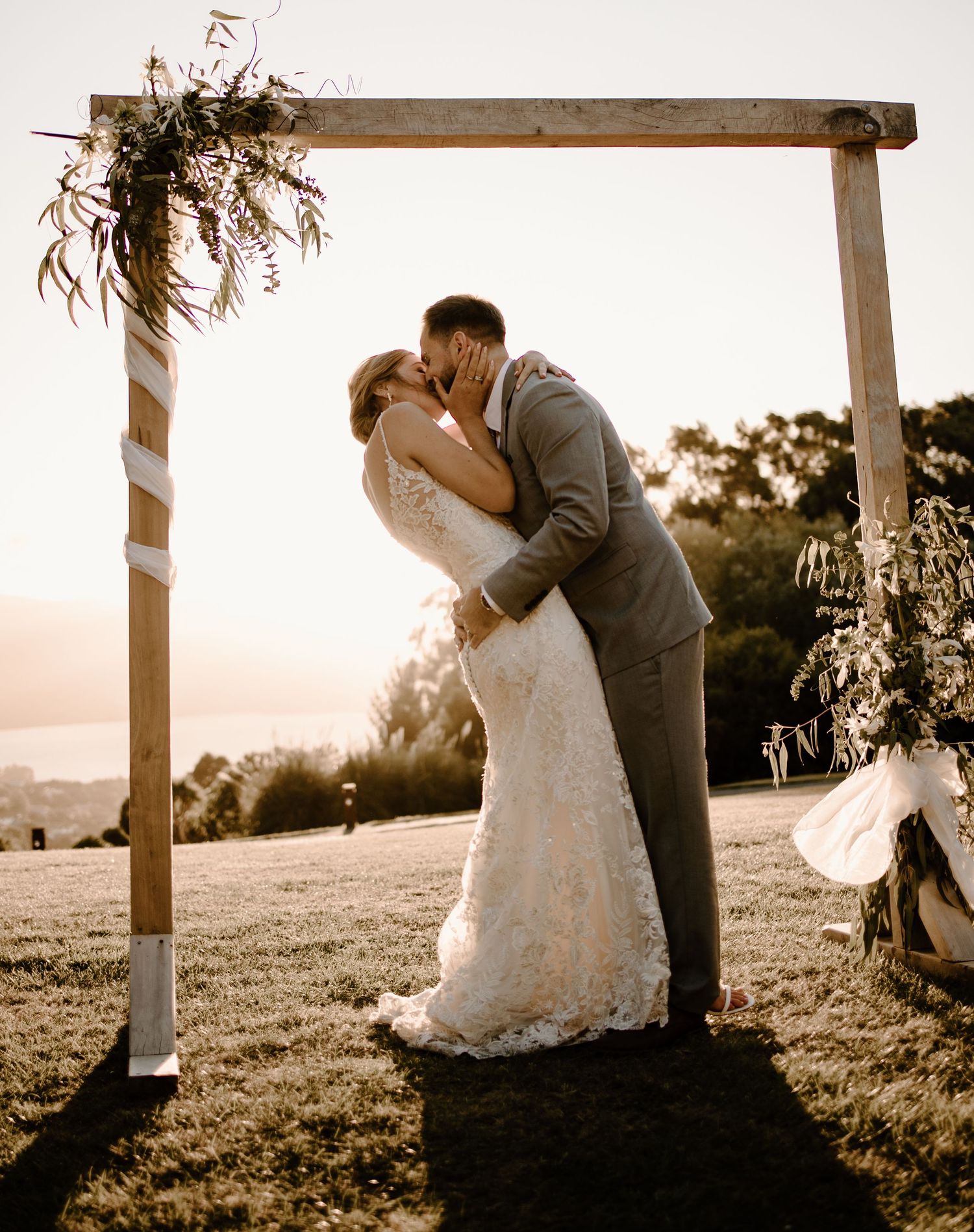 A wedding ceremony arch decorated with floral arrangements frames a romantic moment at sunset.