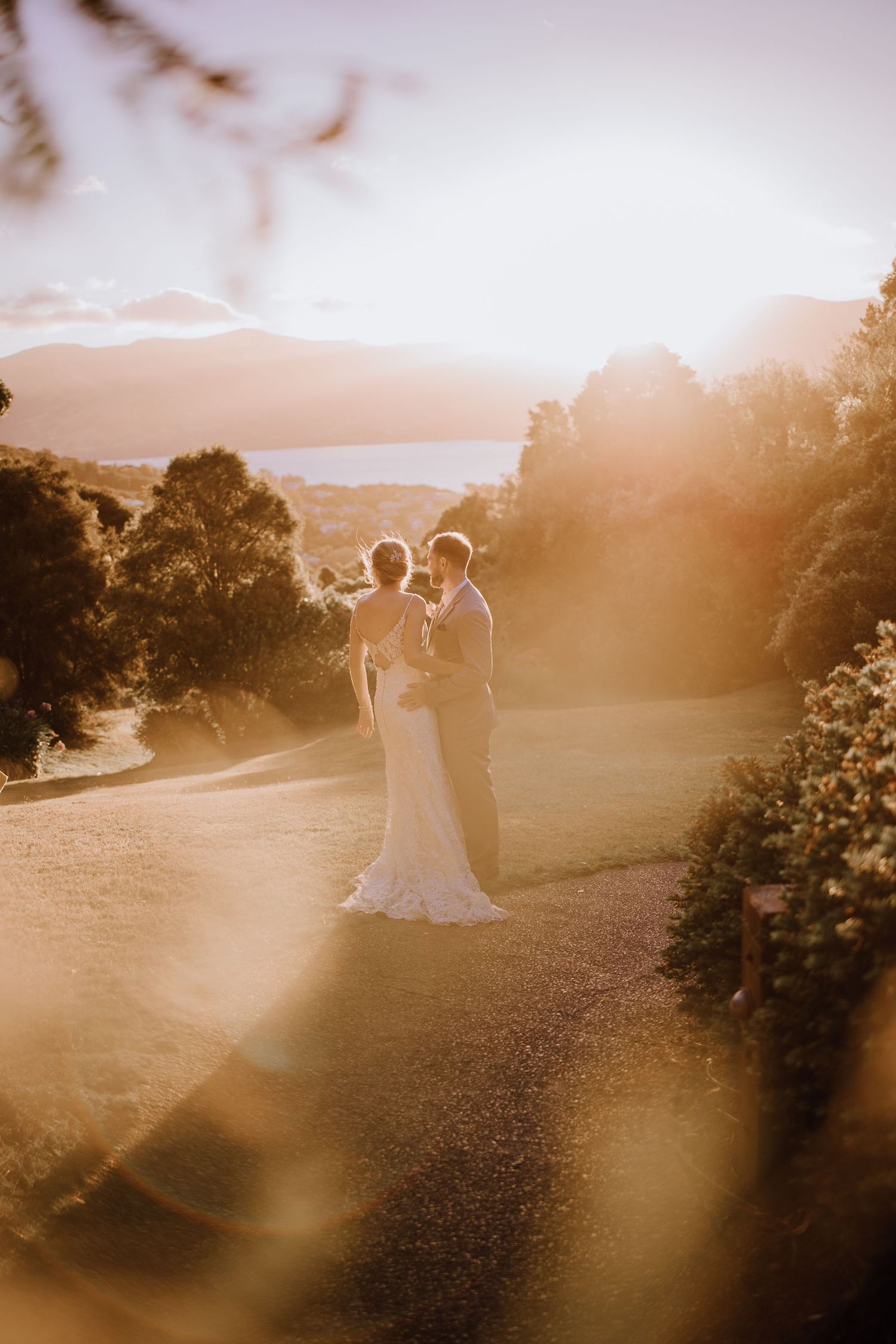 A wedding couple stands together on a scenic overlook during sunset with mountains in the distance.