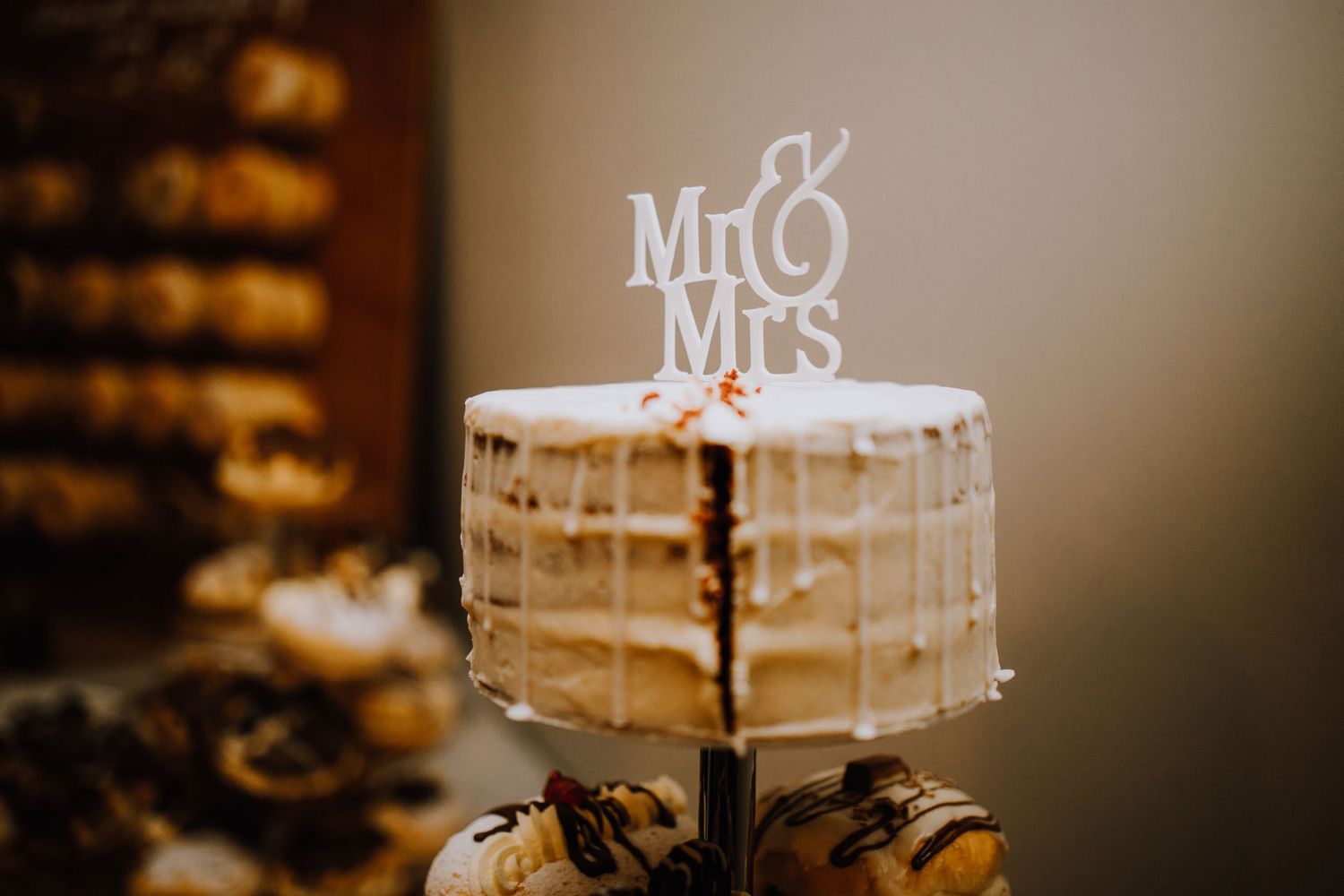 A semi-naked wedding cake topped with Mr & Mrs signage sits on a dessert table.