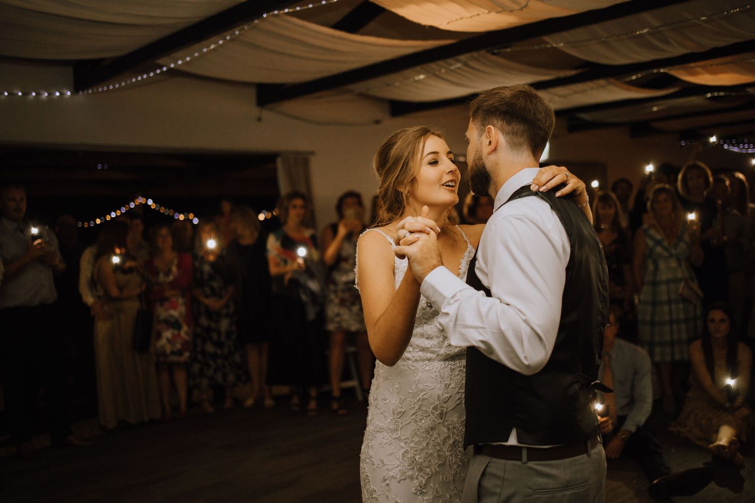 Intimate wedding dance captured in warm lighting with guests watching in background.