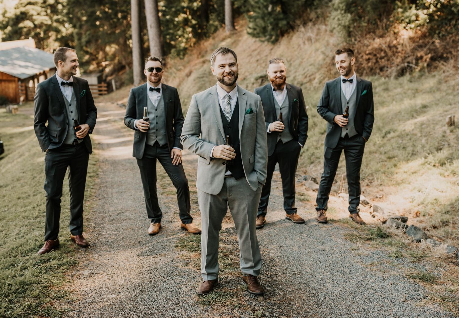 Groomsmen in grey suits walking along an outdoor path at a wedding venue.