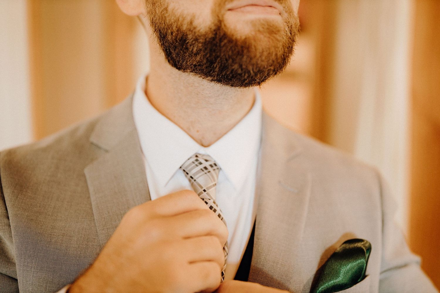 Close-up of a gray suit with patterned tie being adjusted against warm lighting.