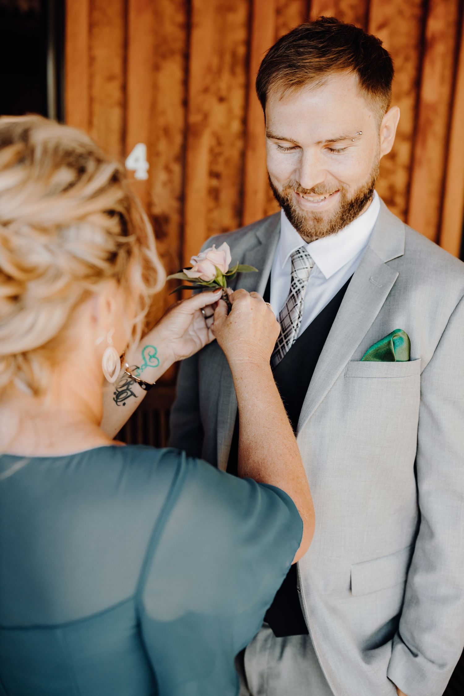 Wedding preparation moment as boutonniere is pinned on light gray suit jacket.