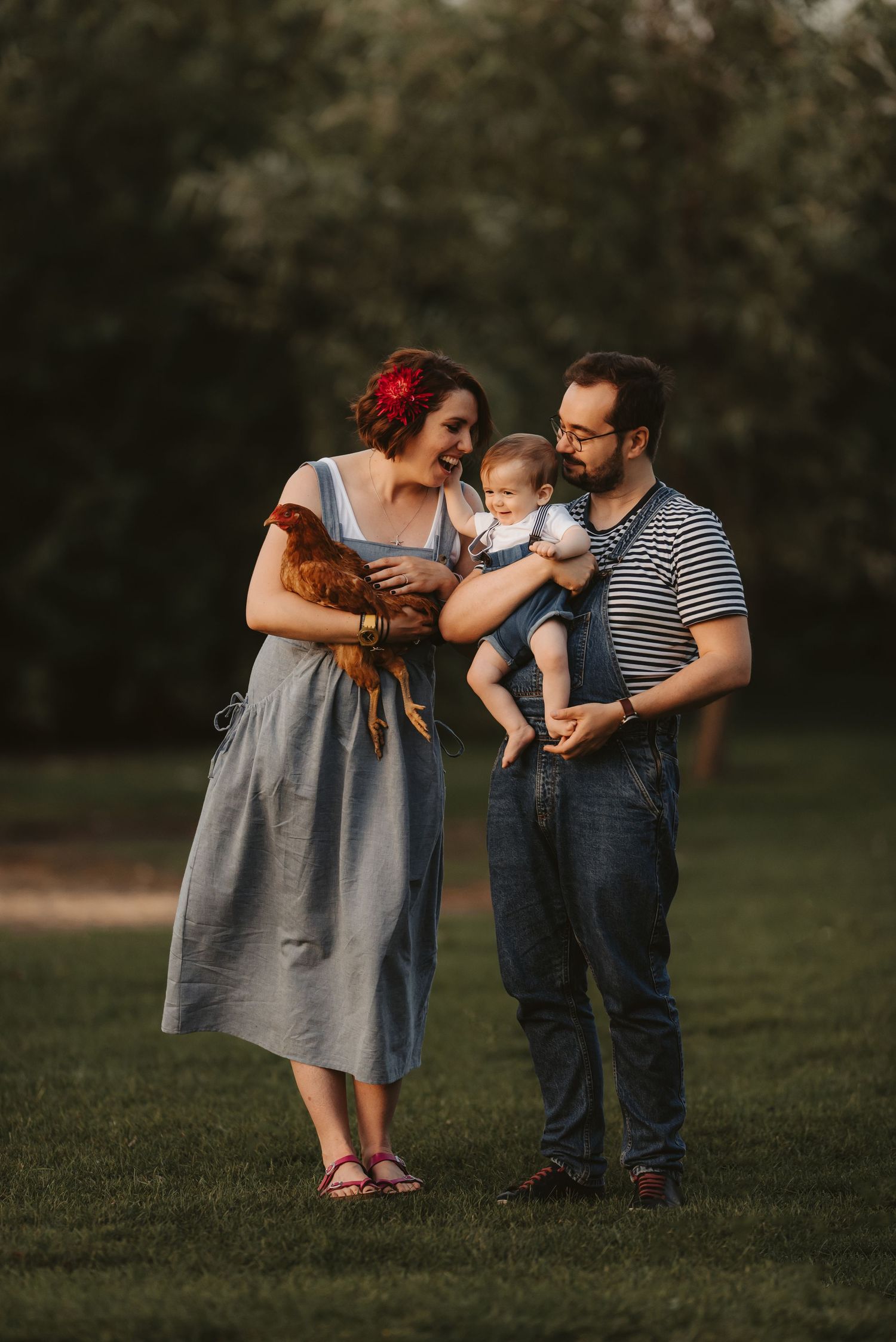 A family in vintage-inspired outfits shares a tender moment together on a grassy field at sunset.