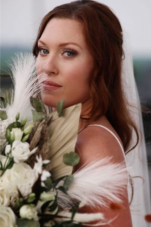 Bridal portrait with white roses and pampas grass bouquet against soft background.