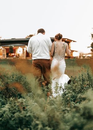 A couple walking through tall greenery during sunset.