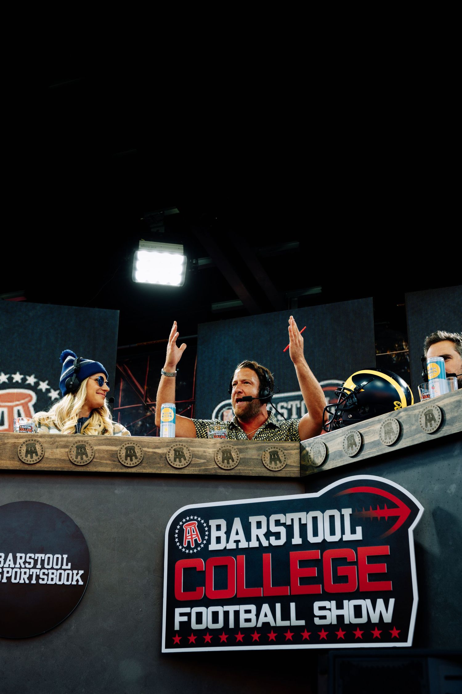Barstool College Football Show stage setup with a logo banner and hosts engaged in live broadcast.