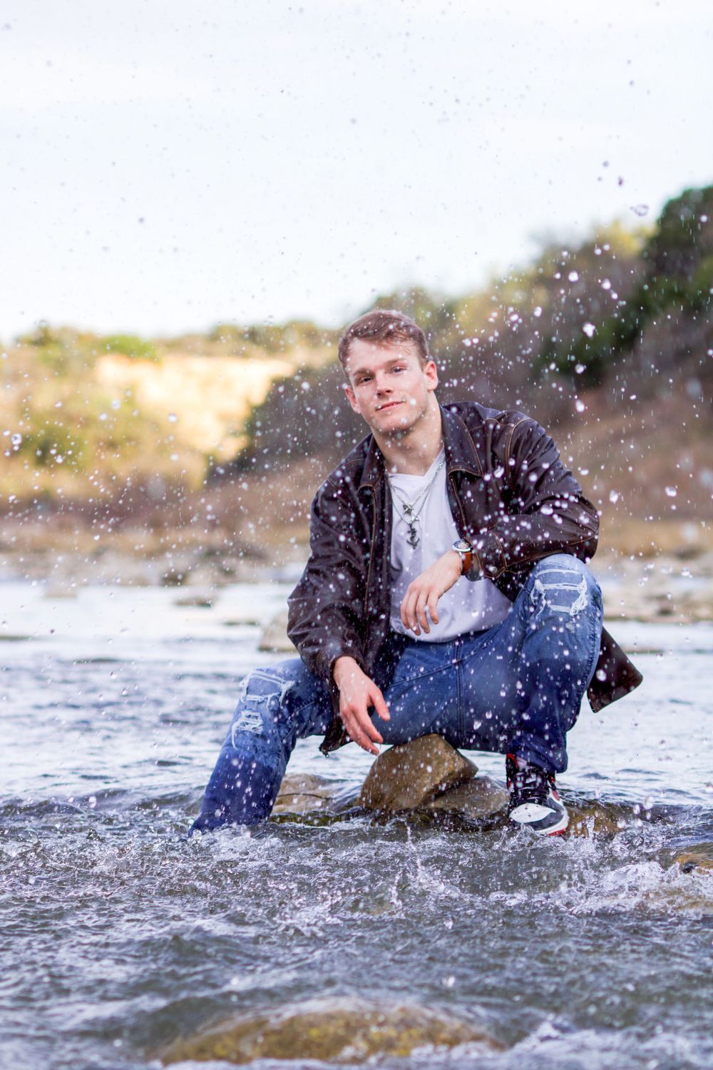 Person poses on rock in stream with water splashing around them.