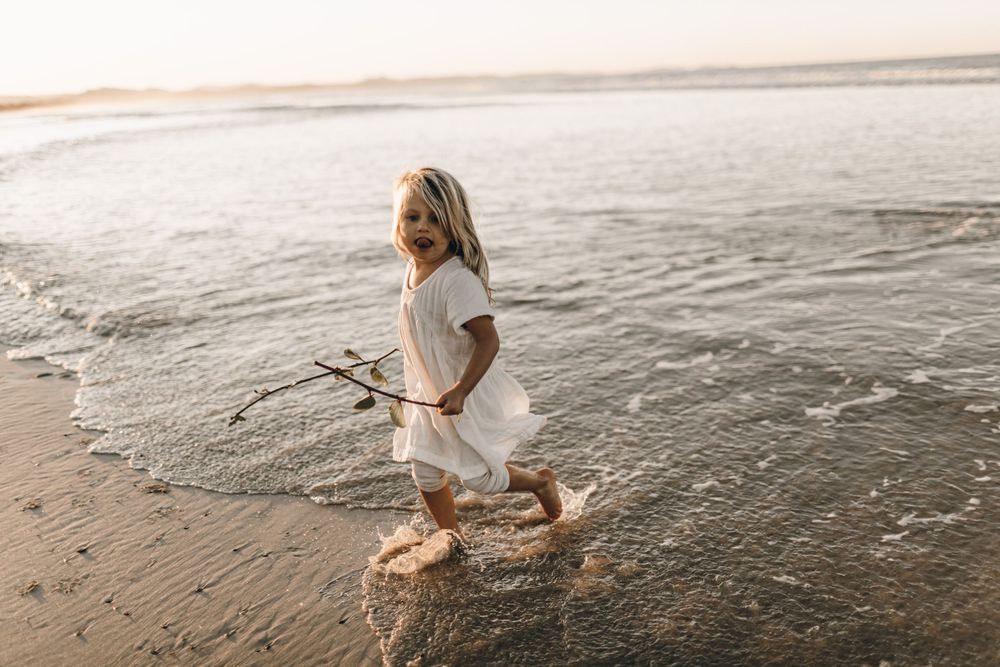 Child playing with a stick while running through shallow ocean waves.
