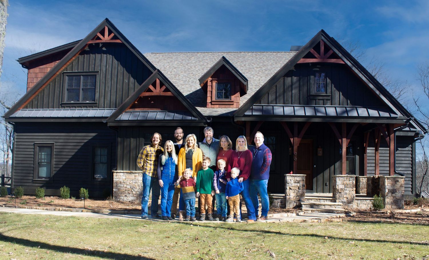 A large group gathered in front of a modern rustic-style house with wooden accents.