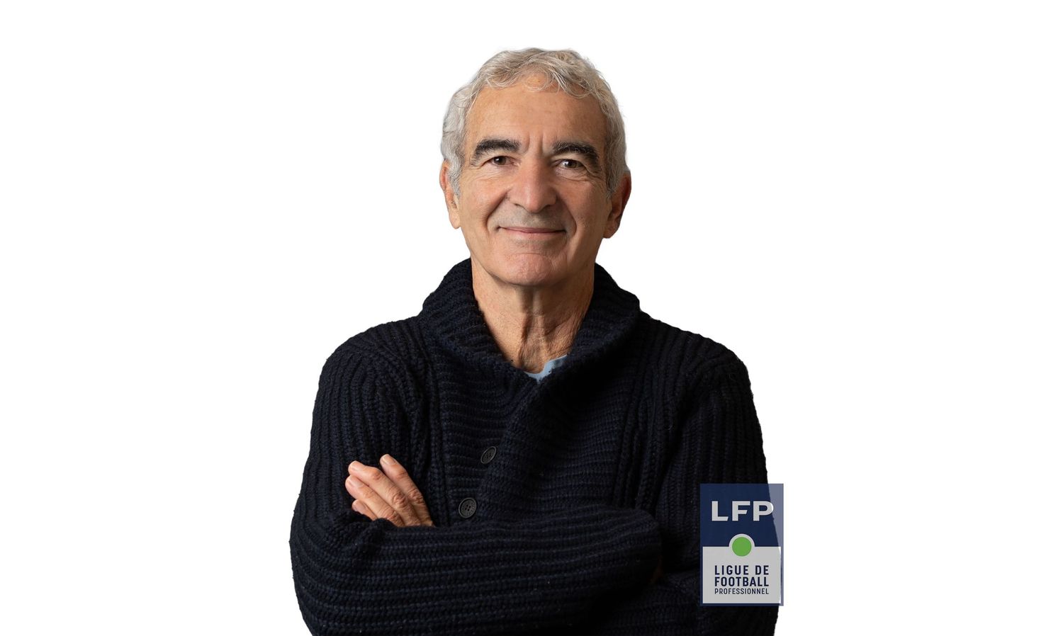 Raymond Domenec wearing a black sweater stands with crossed arms and a warm smile against a light background.