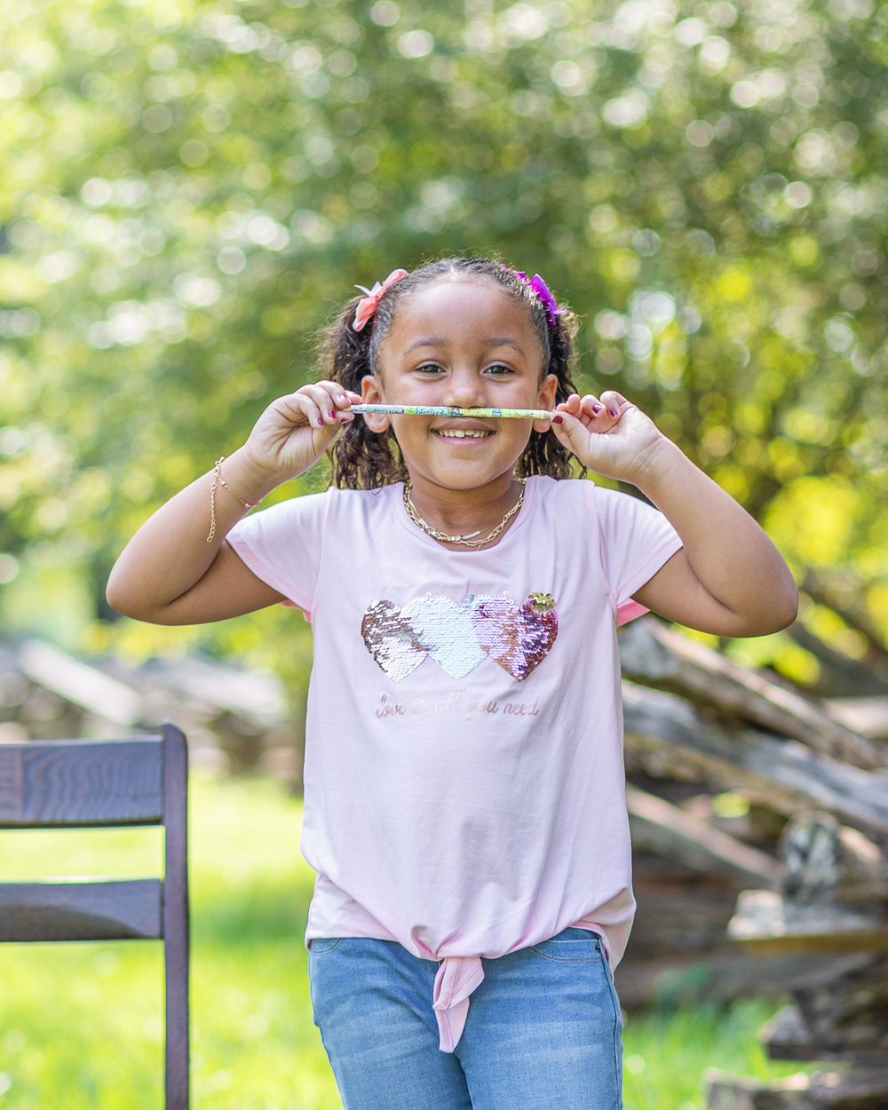 Student in unicorn shirt makes playful mustache gesture with hair while smiling outdoors.