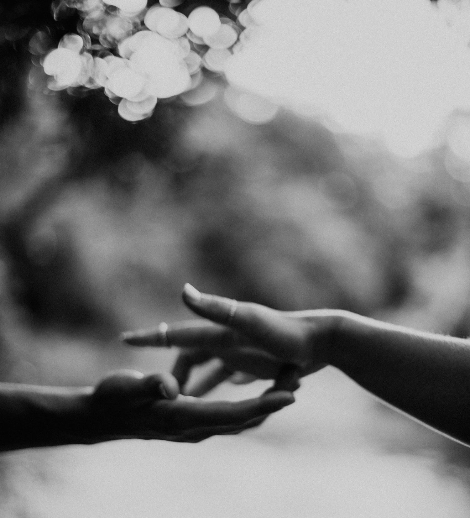 Two hands reaching towards each other in a gentle, ethereal black and white composition with bokeh background.