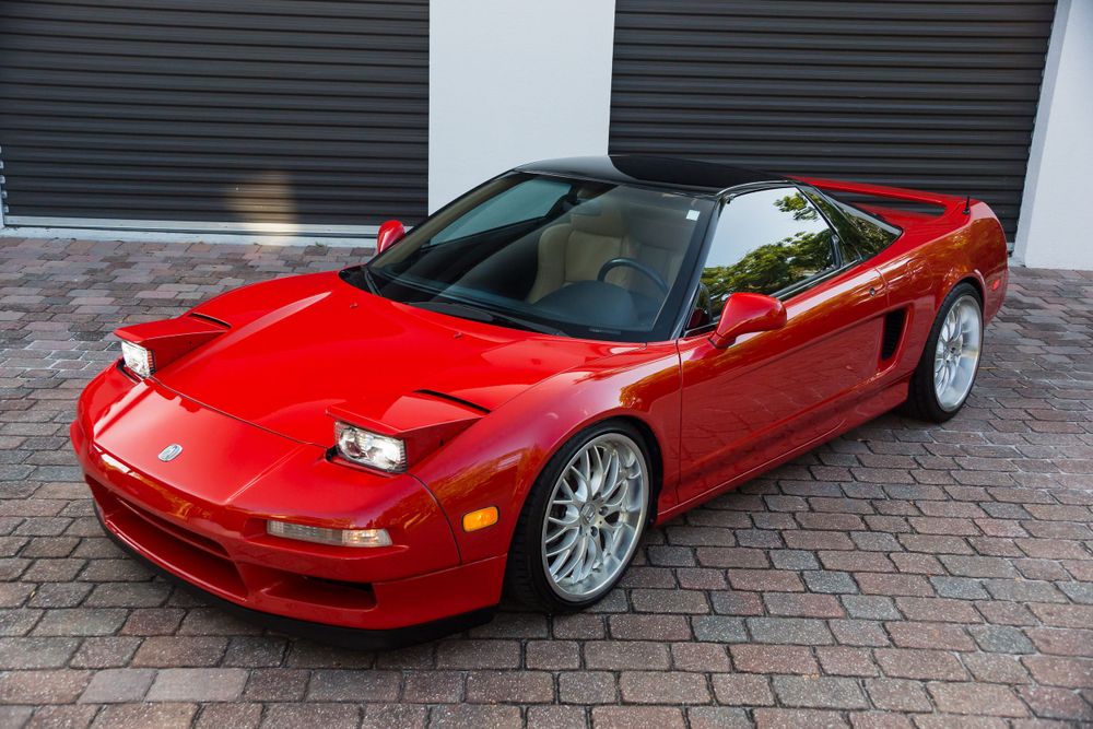 Red Acura NSX convertible with silver wheels photographed in front of garage doors.
