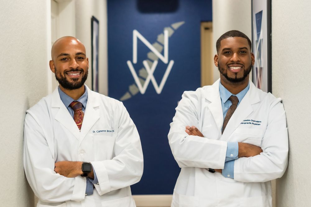 Two healthcare professionals in white coats standing in front of a blue wall with a logo.