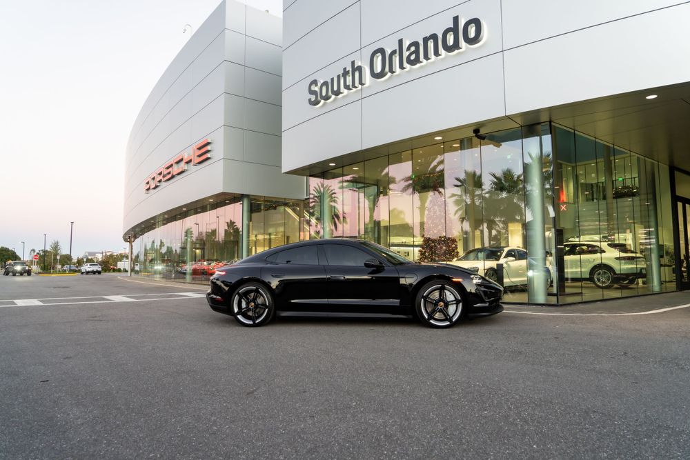 Black luxury sports car parked outside South Orlando Porsche dealership at dusk.