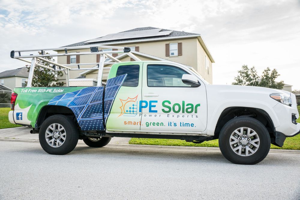 A branded PE Solar company truck with blue and green graphics parked in front of a residential building.