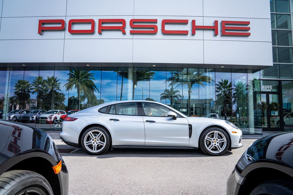 Silver Porsche Panamera sedan profile view displayed at modern dealership with palm trees.