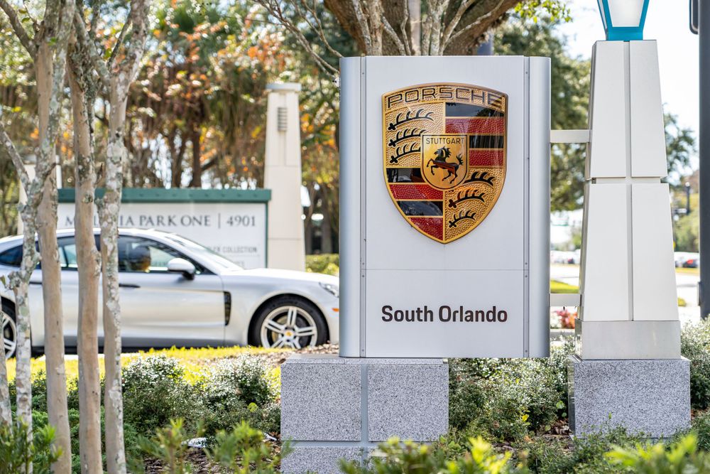 Porsche dealership entrance sign with company logo mounted on stone pillar.