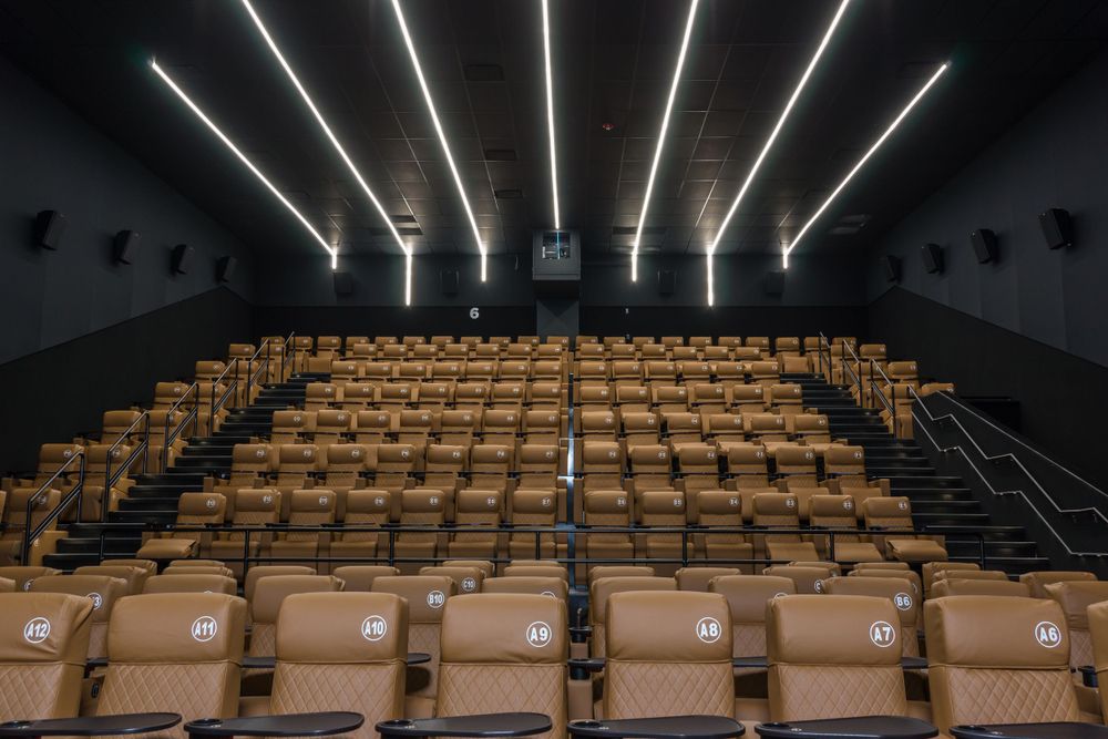 Cinema auditorium featuring geometric ceiling lights and rows of comfortable stadium seating.