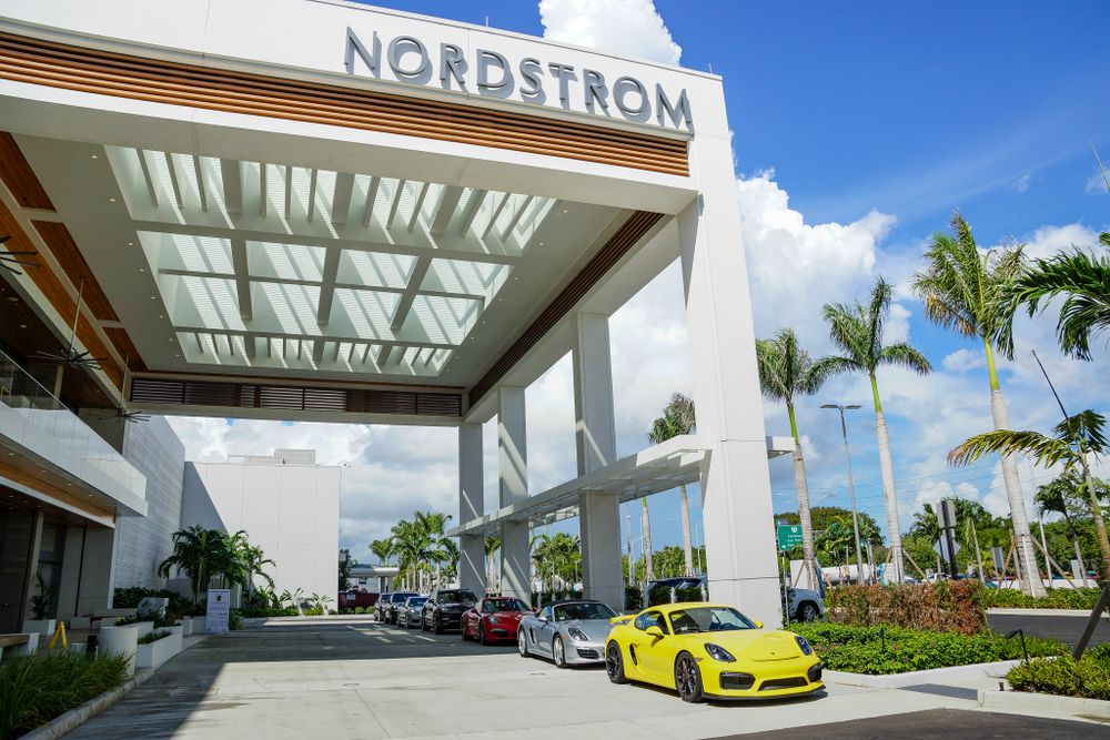 Nordstrom store exterior with palm trees and a yellow sports car parked under a modern canopy.