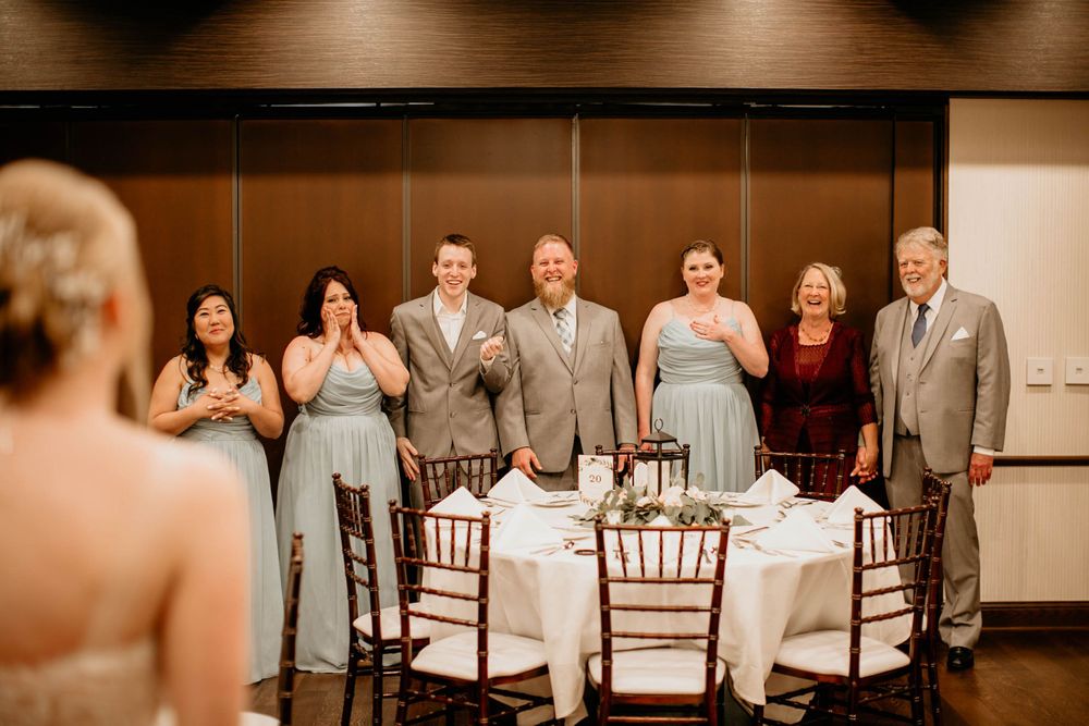 Wedding party guests applaud and smile as bride approaches the sweetheart table during wedding reception.