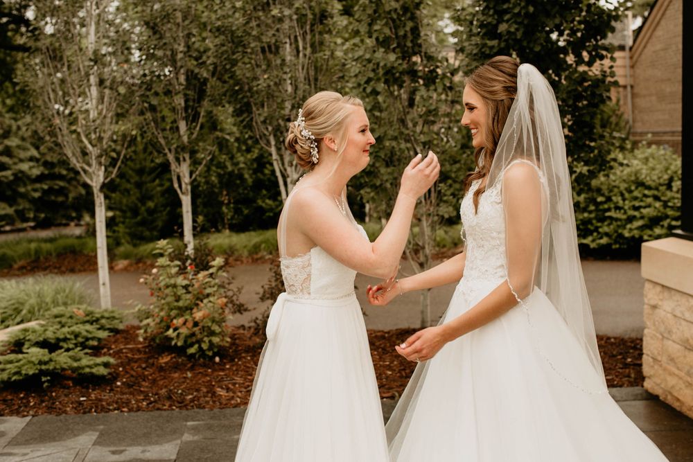 Two brides share a touching moment as one gently touches the others face during their wedding first look.