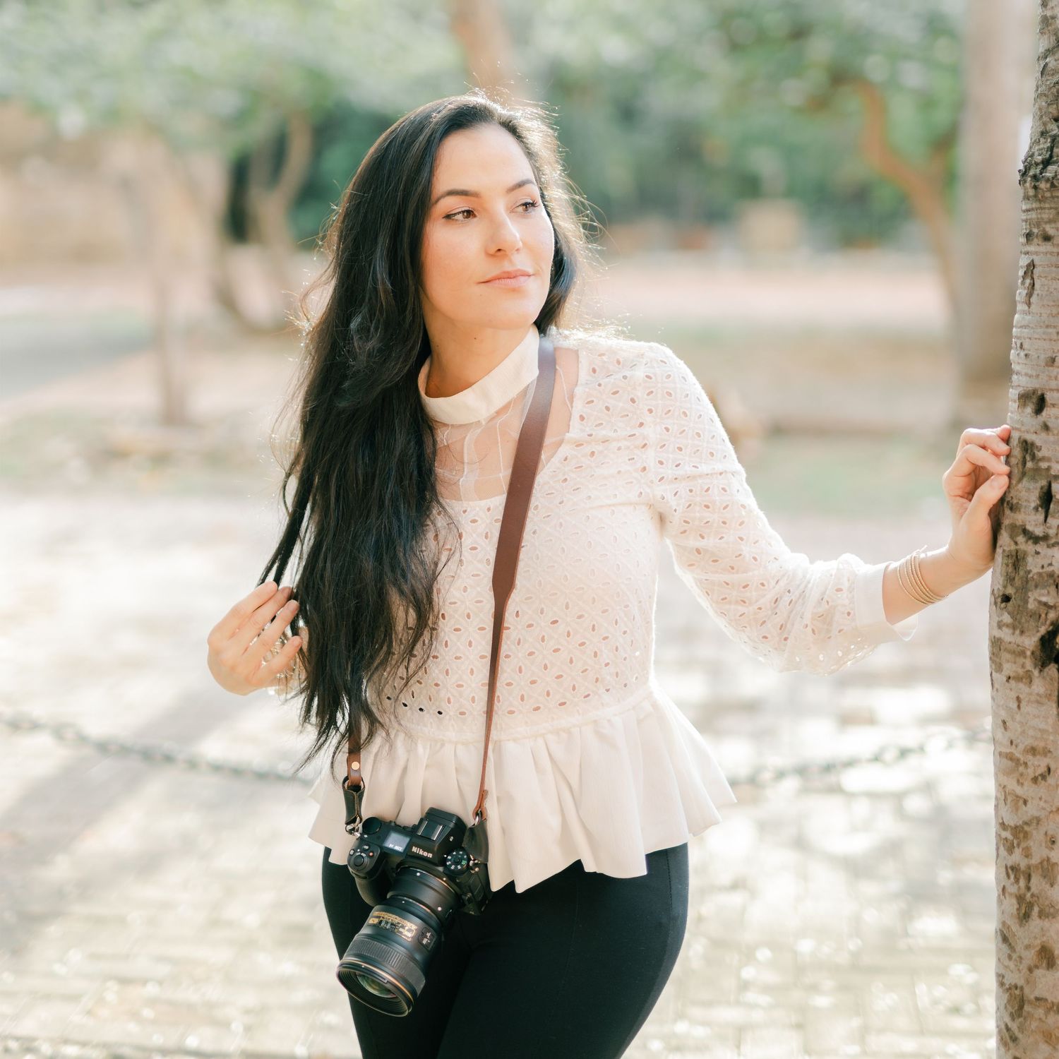 Fine art portrait of photographer in lace blouse with camera in outdoor setting.