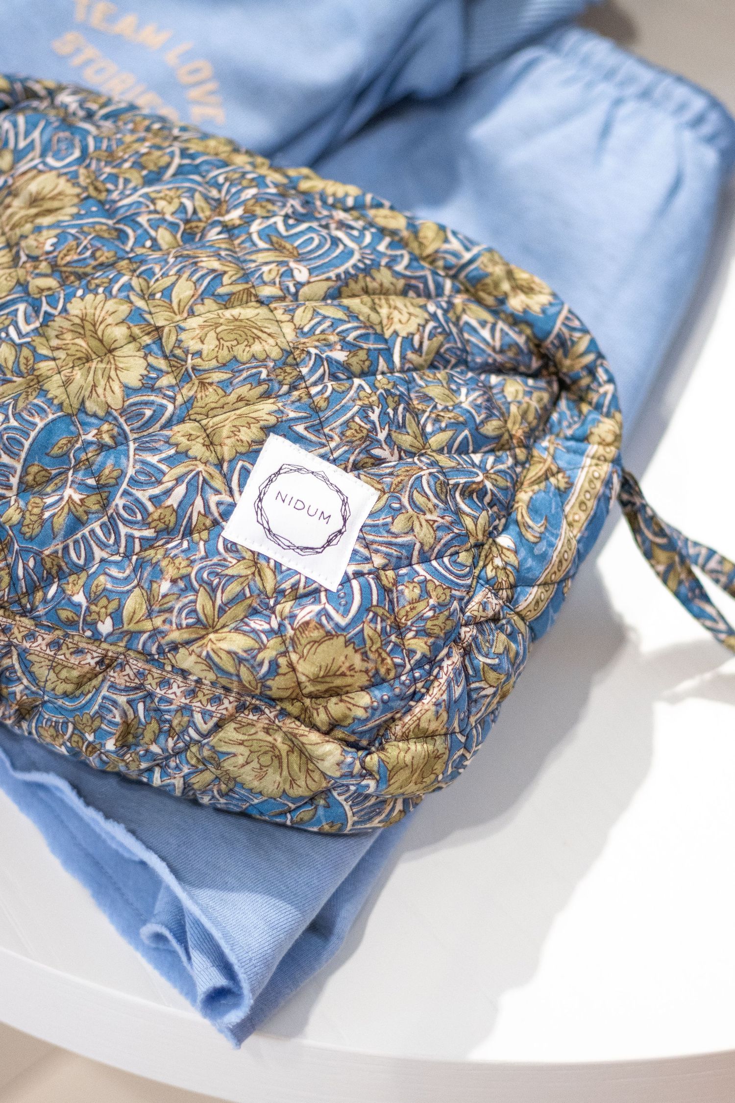 Productfotografie van een blauw gebloemde toilettas met een logo van Nidum er op geborduurd.