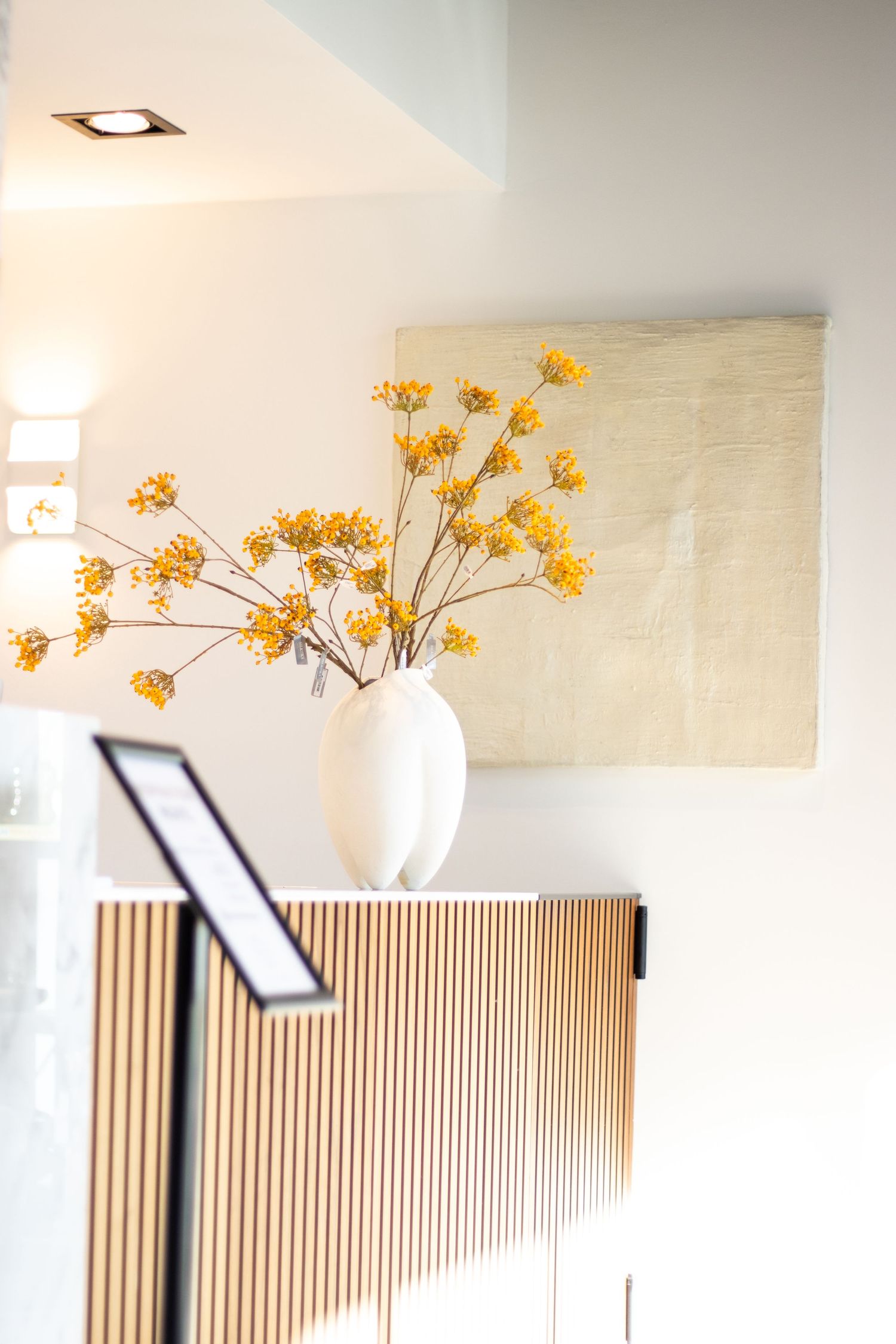 Houten balie met een witte vaas en gele bloemen, witte muren op de achtergrond, ideaal voor moderne interieur- en decorfotografie.
