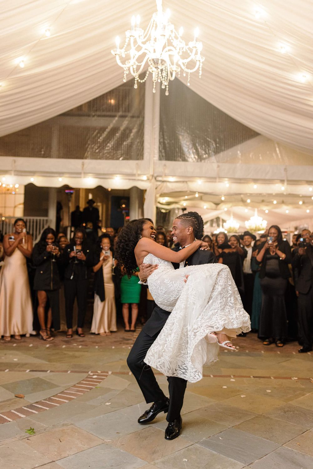 A couple performs their first dance under a crystal chandelier in an elegant tent reception.