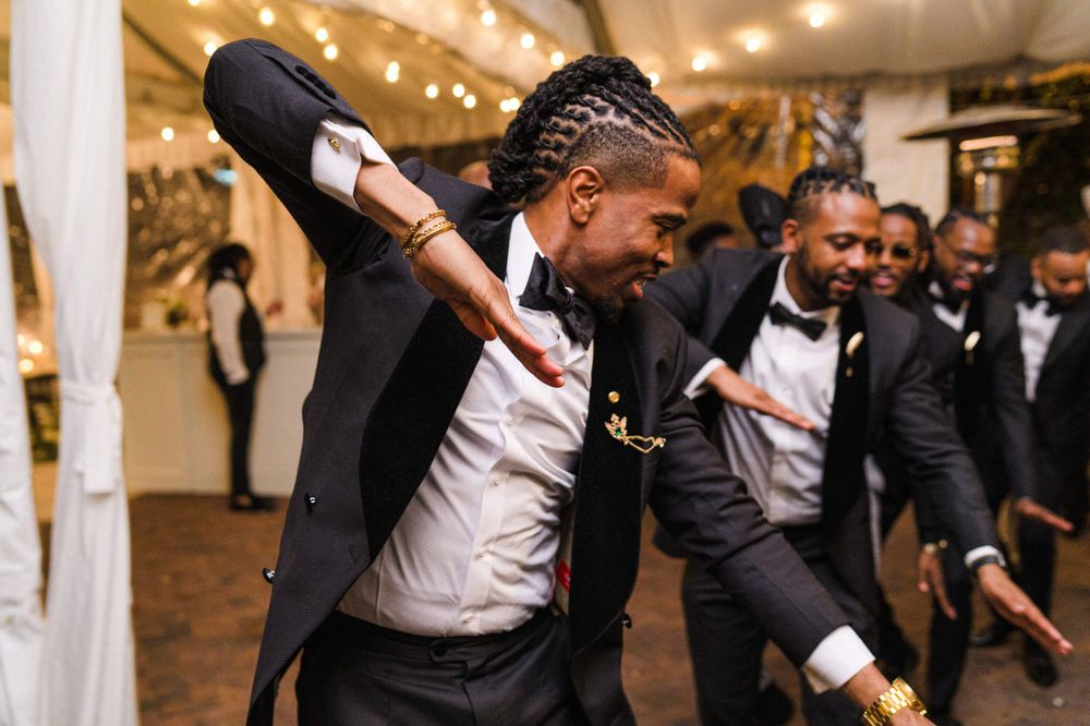 Energetic dance moves on display as guests celebrate at a wedding reception with string lights overhead.