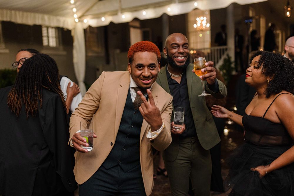 Wedding guests in formal attire enjoying drinks and laughing at an evening reception.