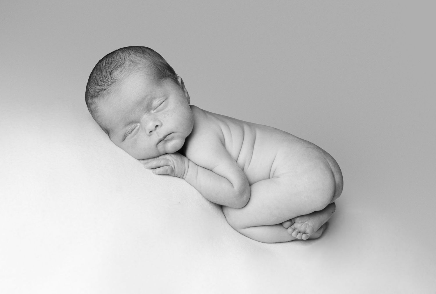 Black and white artistic newborn photography in a curled sleepy pose.