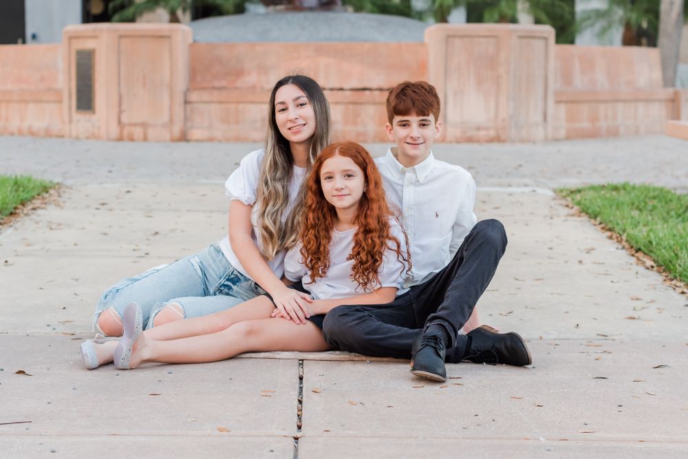 siblings pose together on the ground in front of Lake Mirror in Lakeland, Florida
