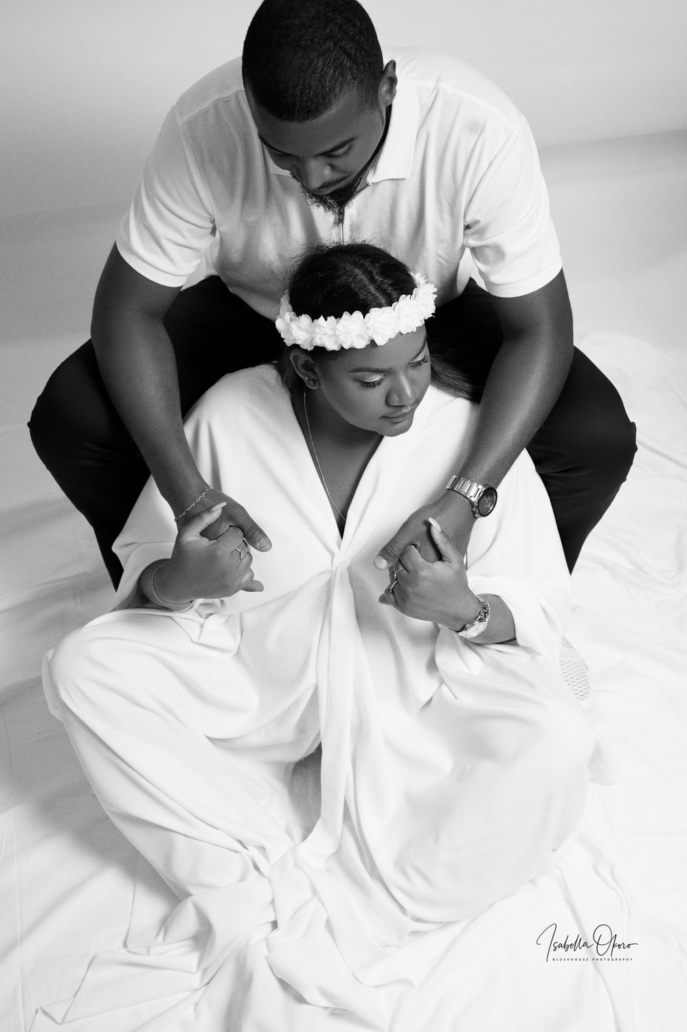 Black and white intimate maternity portrait captured in studio with couple in matching white outfits.