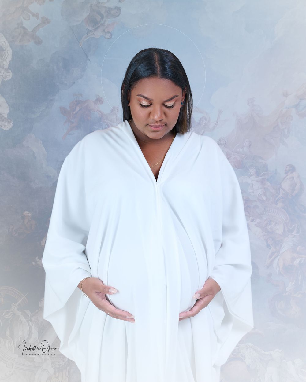 Maternity portrait of woman in white robe against blue backdrop with gentle lighting.